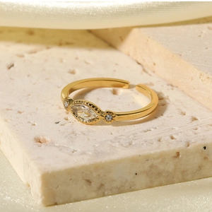 Close-up of a gold adjustable ring with marquise zircon on a beige stone surface