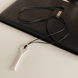 Détail du collier pendentif clé en argent avec cordon noir sur fond de cuir noir