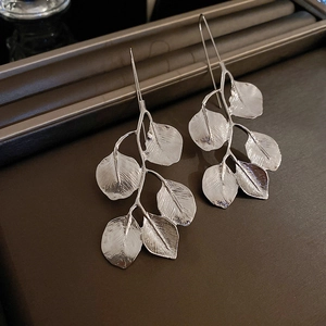 Detailed view of silver leaf-shaped long earrings with metallic finish on dark tray
