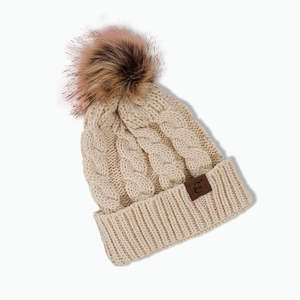 Detail of cable-knit cream beanie showing the pom-pom and stitched leather brand logo