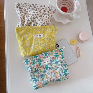 Tre borse cosmetiche in cotone a fiori su una scrivania bianca con accessori
