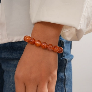 Detail shot of orange translucent acrylic beaded bracelet worn on wrist with casual outfit
