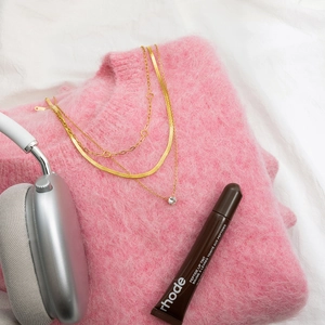 Close-up of gold layered necklace with crystal pendant on pink sweater and accessories
