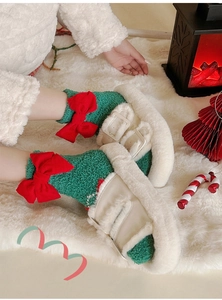 Détail de chaussons en peluche et chaussettes en tricot vert avec nœuds rouges sur tapis doux