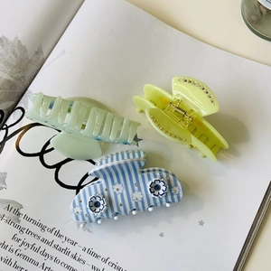 Détail de pinces à cheveux en acétate avec fleurs, strass et motifs rayés sur un magazine