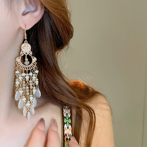 Close-up of Bohemian gold tassel earrings with moon geometry and droplets on model