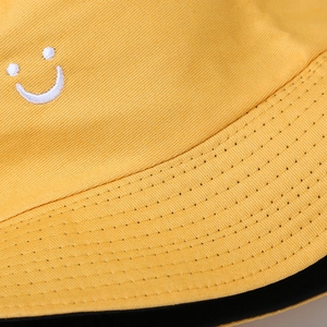 Detailed close-up of white smiley face embroidery on high-quality yellow cotton bucket hat