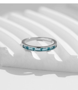 Detail view of silver ring featuring channel-set rectangular blue gemstones on white stand