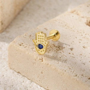Macro view of gold Hamsa hand labret stud with blue gemstone eye on beige stone