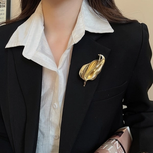 Close-up of a gold metal leaf brooch with textured folds on a black suit lapel