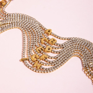 Macro shot of 18K gold letter pendants with white zircon pavé on thin chains