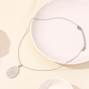 Silver stainless steel Tree of Life pendant necklace on a white porcelain plate