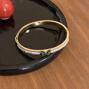 Detailed view of a gold-plated bangle featuring white zircons and a green butterfly charm