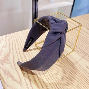 Detail of dark grey fabric wide knotted headband with a sewn Handmade label on a metal stand