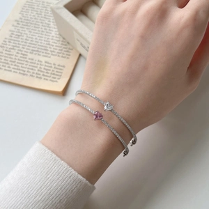 Detail of silver bangles with white and pink heart zircons worn on female wrist