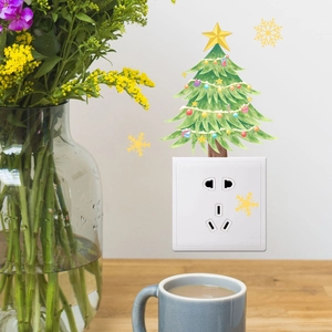 Close-up of a festive cartoon Christmas tree sticker applied above a white wall socket