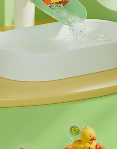 Detail of cute yellow duck on green water slide with water splashing into white pool basin