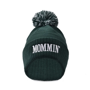 Close-up of MOMMIN' 3D embroidery on a dark green knitted beanie with pom-pom