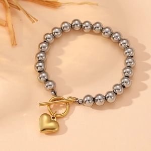 Bracelet à billes argentées avec pendentif cœur doré et fermoir à bascule sur fond beige
