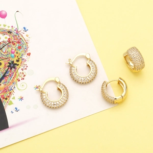 U-shaped gold huggie earrings with cubic zirconia pavé on a minimalist background
