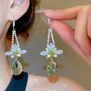 Detail of gold flower drop earrings with green zircon pendants on model's ear