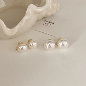 Detail of white pearl earrings with golden mosquito coil clips on a textured tray