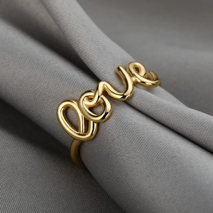Makro-Detail des 18K Goldrings mit Love-Schriftzug auf elegantem grauem Satinstoff