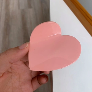 Close-up of a sweet heart-shaped pink hair claw clip held by hand showing glossy finish