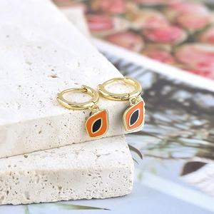 Macro shot of gold hoop earrings featuring orange and black enamel fruit charms on stone