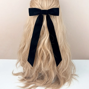 Elegant black velvet bow hair clip with long ribbons shown on a woman's hair