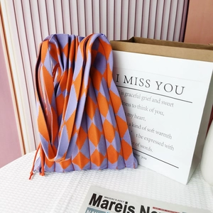 Detail of purple and orange pleated knit bag with diamond pattern on white grid fabric