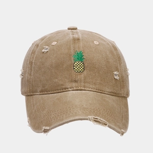 Close-up of pineapple embroidery and distressed ripped details on khaki baseball cap