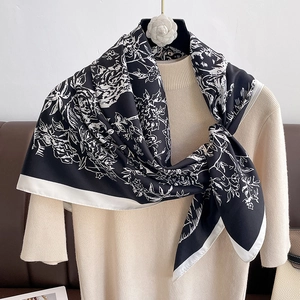 Dettaglio della sciarpa in seta con motivo floreale bianco e nero su maglione beige