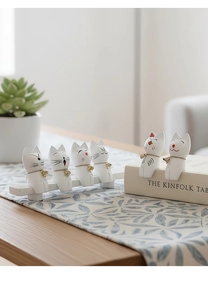 Close-up of six white ceramic cat figurines with gold bells on a wooden base