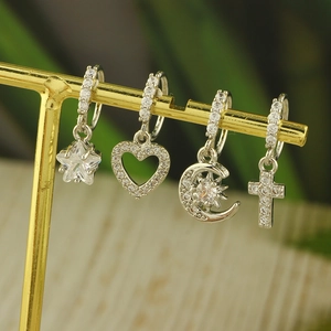 Detail of four silver piercing rings with star, heart, moon and cross zircon pendants