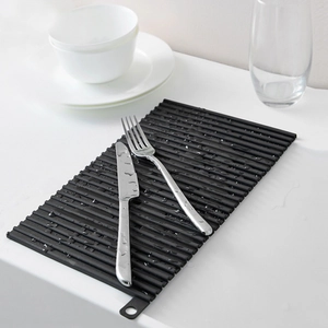 Black silicone drying mat with wave stripes on white counter with cutlery and glass
