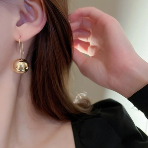 Close-up of golden spherical drop earring with polished metallic finish on a model