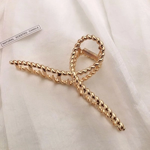 Macro view of gold twisted metal hair claw clip on soft white draped fabric