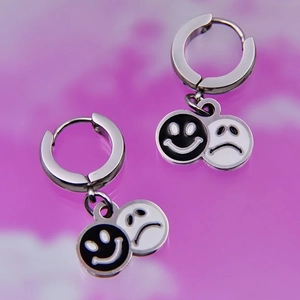 Detail of stainless steel hoop earrings featuring black and white emoji face charms