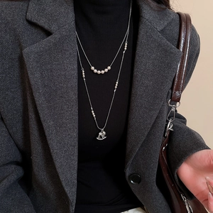 Detail of double-layer necklace with white pearls and a crystal-encrusted rocking horse