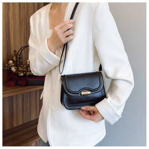 Detail of a vintage black leather crossbody bag with a gold spiral lock on a white blazer