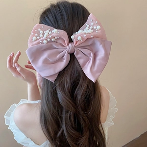 Detailed view of pink satin bow hair clip with delicate pearls on elegant hairstyle
