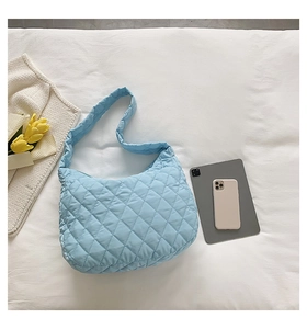Close-up of light blue quilted hobo bag with padded strap on white bedding context