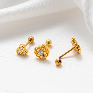 Close-up of gold zircon ear studs with screw ball backs on white silk fabric background