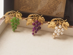 Macro shot of three vintage grape brooches in green, purple, and white on a wooden box