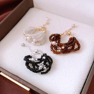 Close-up of three multilayer beaded rings in white, brown, and black with faux pearls