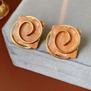 Detailed macro view of vintage square enamel earrings with gold spiral accents on suede