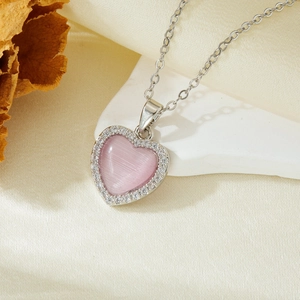 Detailed close-up of a silver heart pendant necklace with a pink cat eye stone on silk