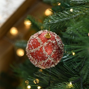 Red Christmas ball with gold mesh and beads hanging on a green festive tree branch