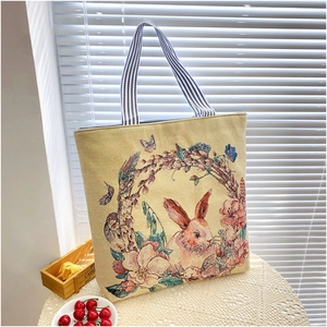 Detail view of a beige canvas tote bag featuring an embroidered floral rabbit design